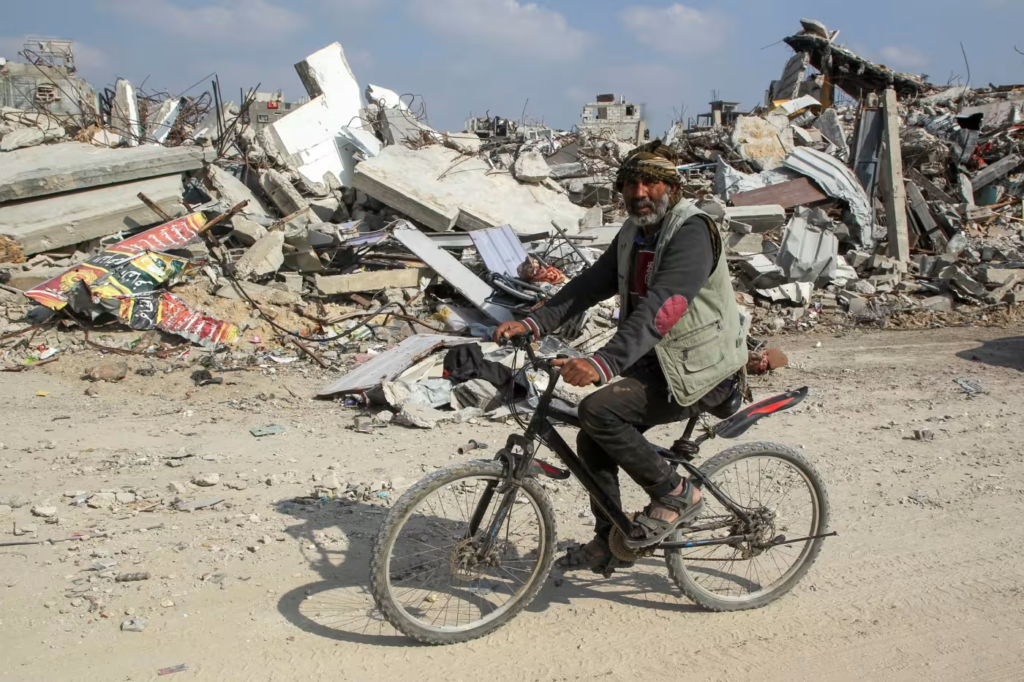 A man rides a bicycle past the rubble of a house in Rafah destroyed during the Israeli offensive © Hatem Khaled/Reuters
