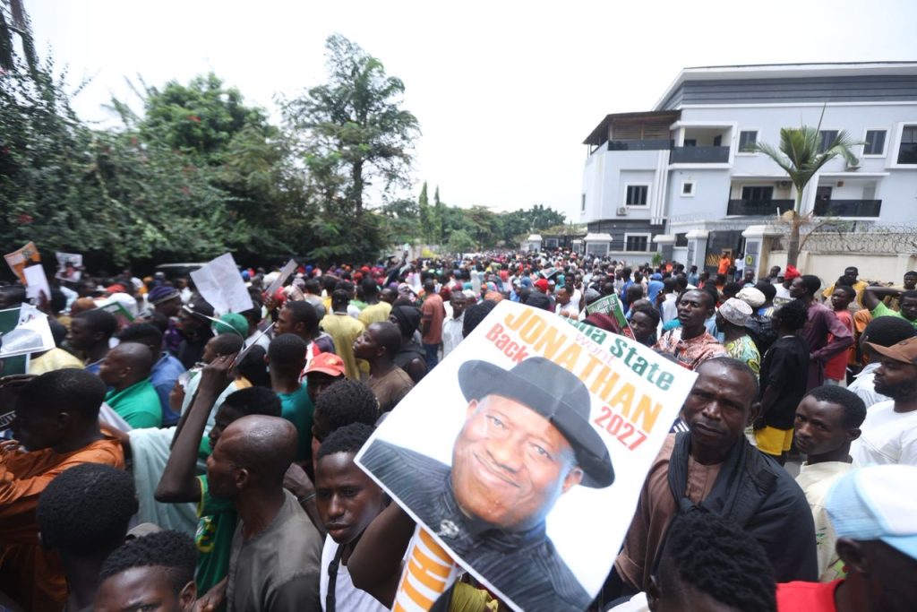 Youths protest in Abuja, urge Goodluck Jonathan to run in 2027 Crowd of Nigerian youths holding placards outside Goodluck Jonathan’s Abuja residence calling for his return to politics.